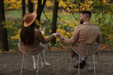 Photo of Happy young couple spending time together in autumn park, back view