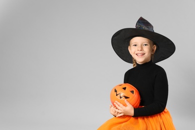 Photo of Cute little girl with pumpkin candy bucket wearing Halloween costume on grey background. Space for text