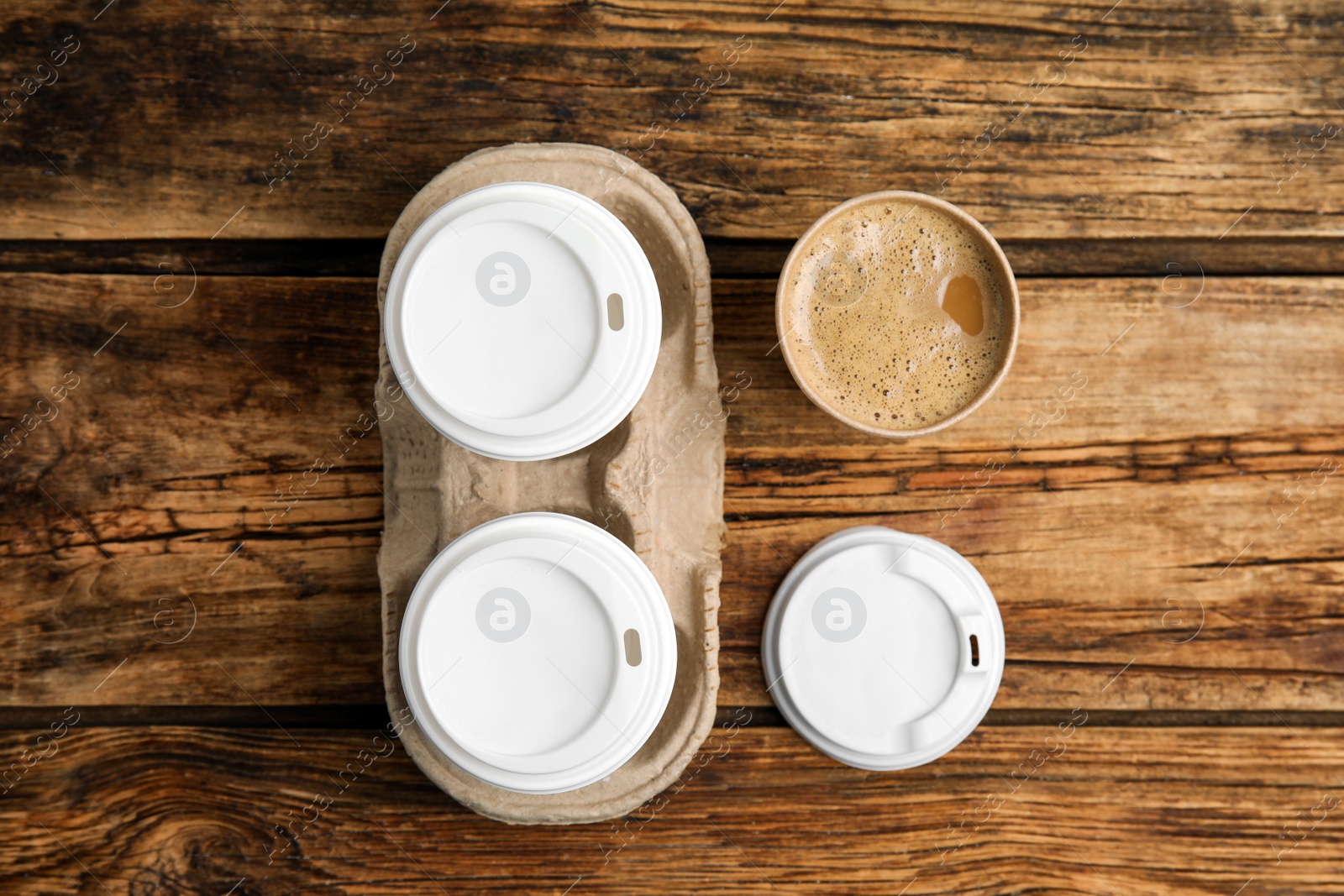 Photo of Takeaway paper coffee cups and cardboard holder on wooden table, flat lay