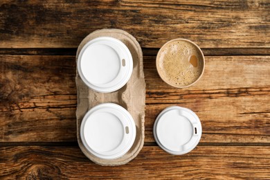 Takeaway paper coffee cups and cardboard holder on wooden table, flat lay