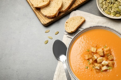 Tasty creamy pumpkin soup served with bread and seeds on grey table, flat lay. Space for text