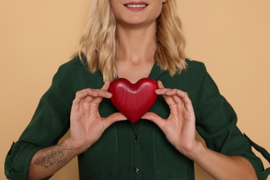 Happy volunteer holding red heart with hands on beige background, closeup
