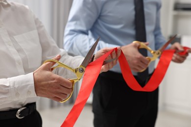 Photo of People cutting red ribbon with scissors indoors, closeup