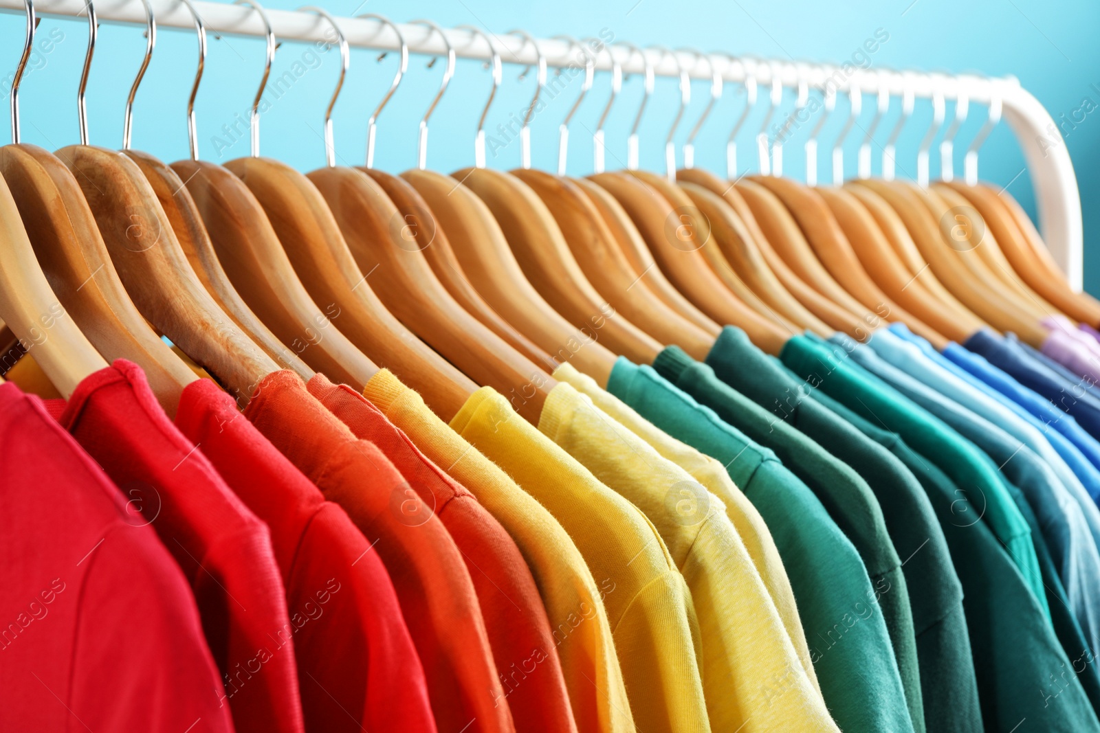 Photo of Rack with bright clothes on blue background. Rainbow colors