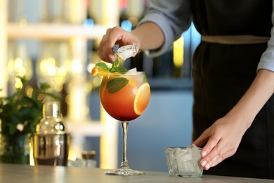 Woman preparing fresh alcoholic cocktail with orange and mint at bar counter, closeup