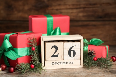 Photo of Block calendar with Boxing Day date near gifts on wooden table