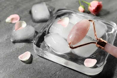 Photo of Natural jade face roller and ice cubes on grey background, closeup