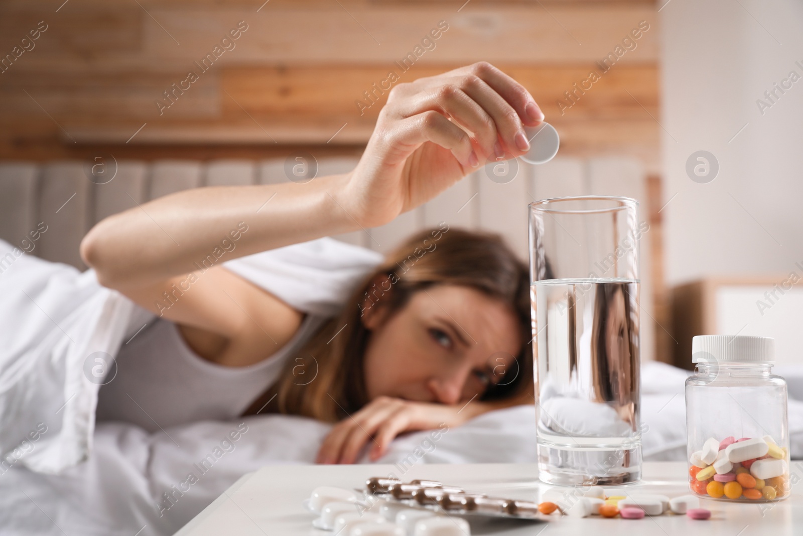 Photo of Woman putting medicine for hangover into glass of water at home, focus on hand with pill