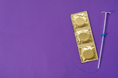 Photo of Contraception choice. Condoms and intrauterine device on purple background, flat lay. Space for text
