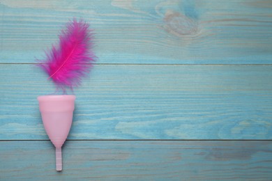 Photo of Menstrual cup and pink feather on turquoise wooden background, flat lay. Space for text