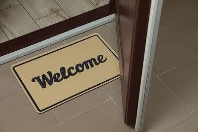 Photo of Beautiful beige doormat with word Welcome on floor near entrance