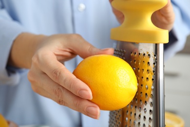 Woman zesting fresh lemon indoors, closeup view