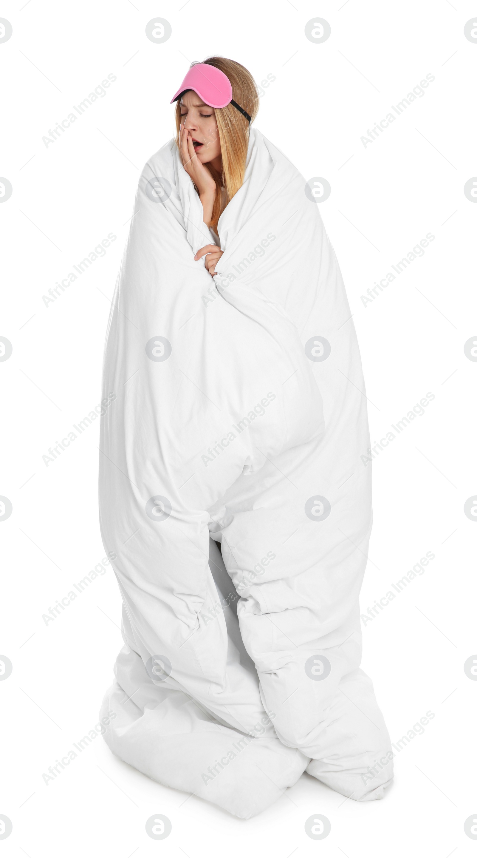 Photo of Young woman in sleeping mask wrapped with soft blanket yawning on white background