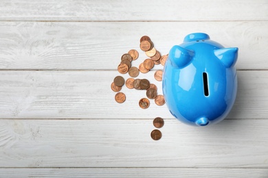 Cute piggy bank and coins on wooden background, top view with space for text