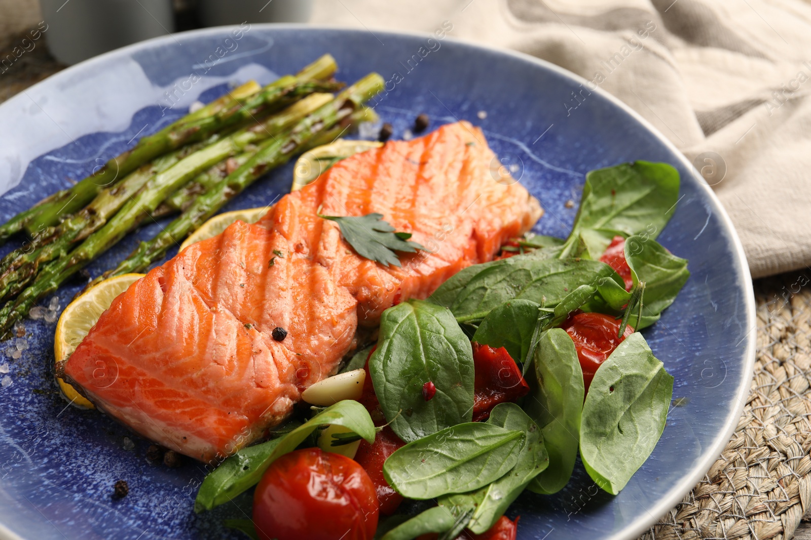 Photo of Tasty grilled salmon with tomatoes, asparagus, spinach and spices on table, closeup