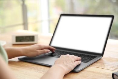 Photo of Woman working with modern laptop at wooden table, closeup. Space for design