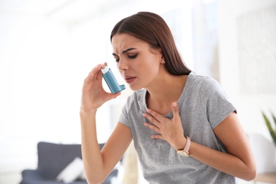 Photo of Young woman with asthma inhaler in light room