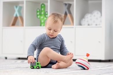 Children toys. Cute little boy playing with car and spinning top on rug at home