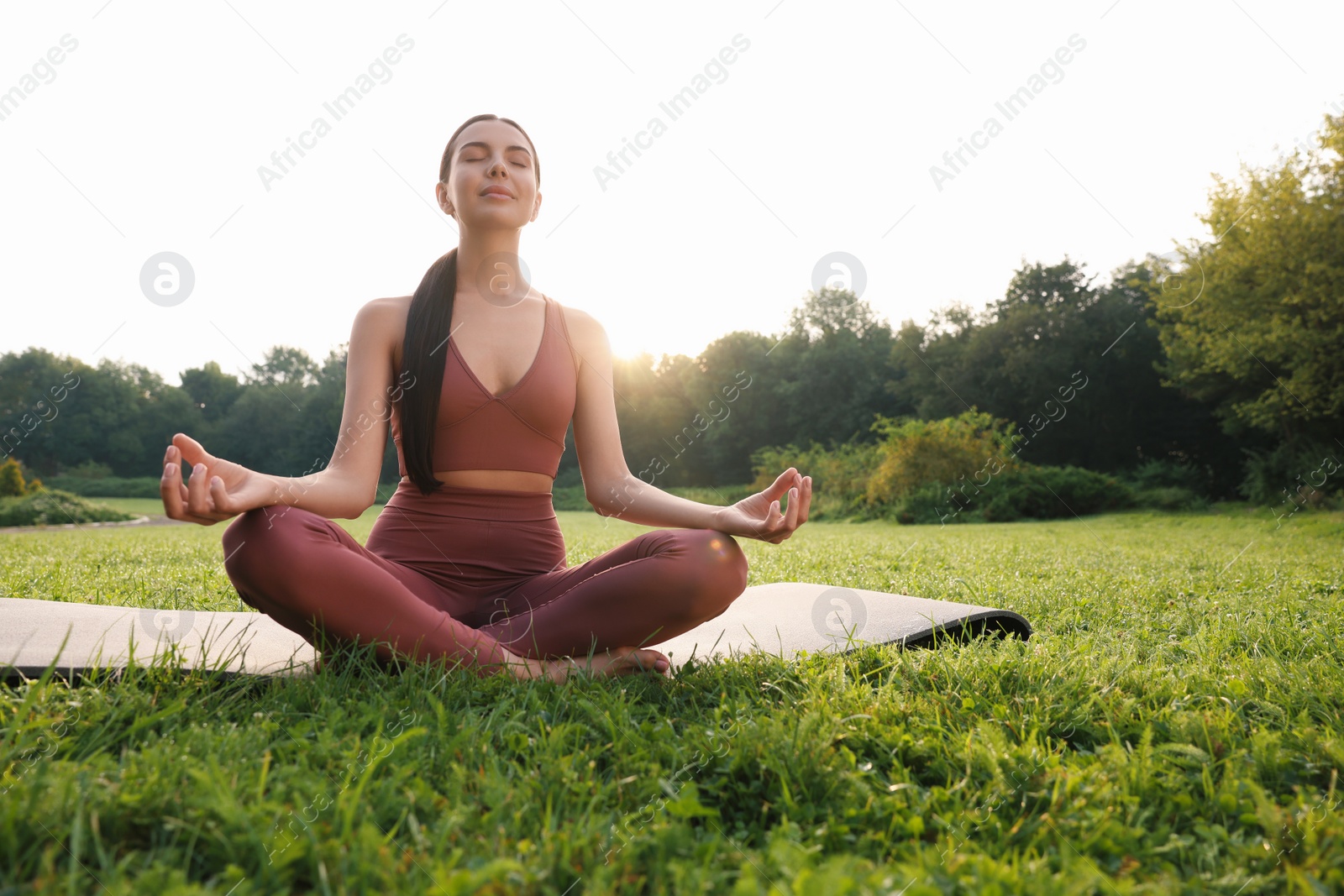 Photo of Beautiful young woman practicing Padmasana on yoga mat outdoors, low angle view. Lotus pose