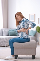 Photo of Young woman suffering from back pain at home