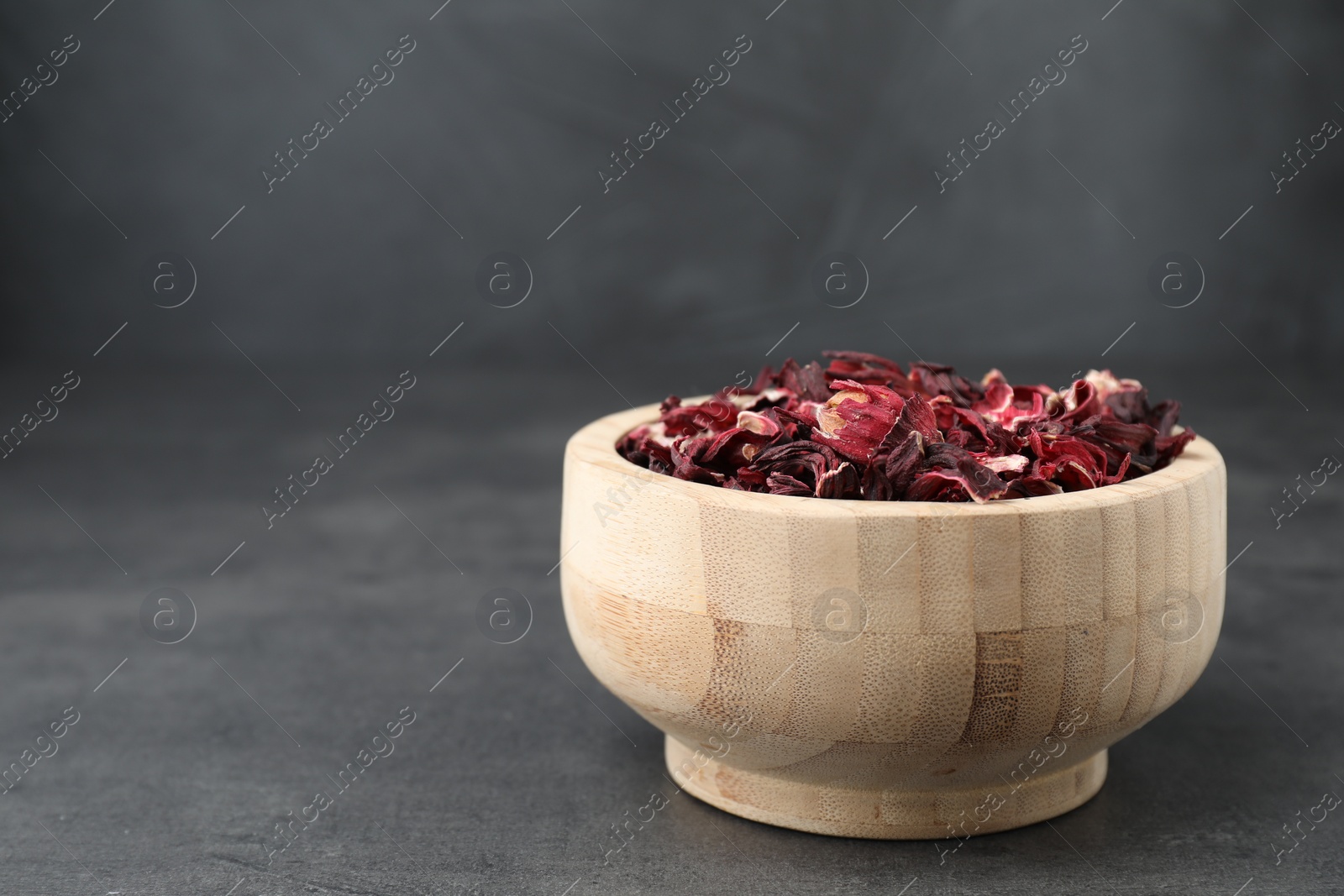 Photo of Hibiscus tea. Wooden bowl with dried roselle calyces on grey table. Space for text