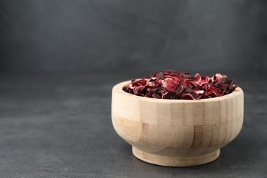 Hibiscus tea. Wooden bowl with dried roselle calyces on grey table. Space for text