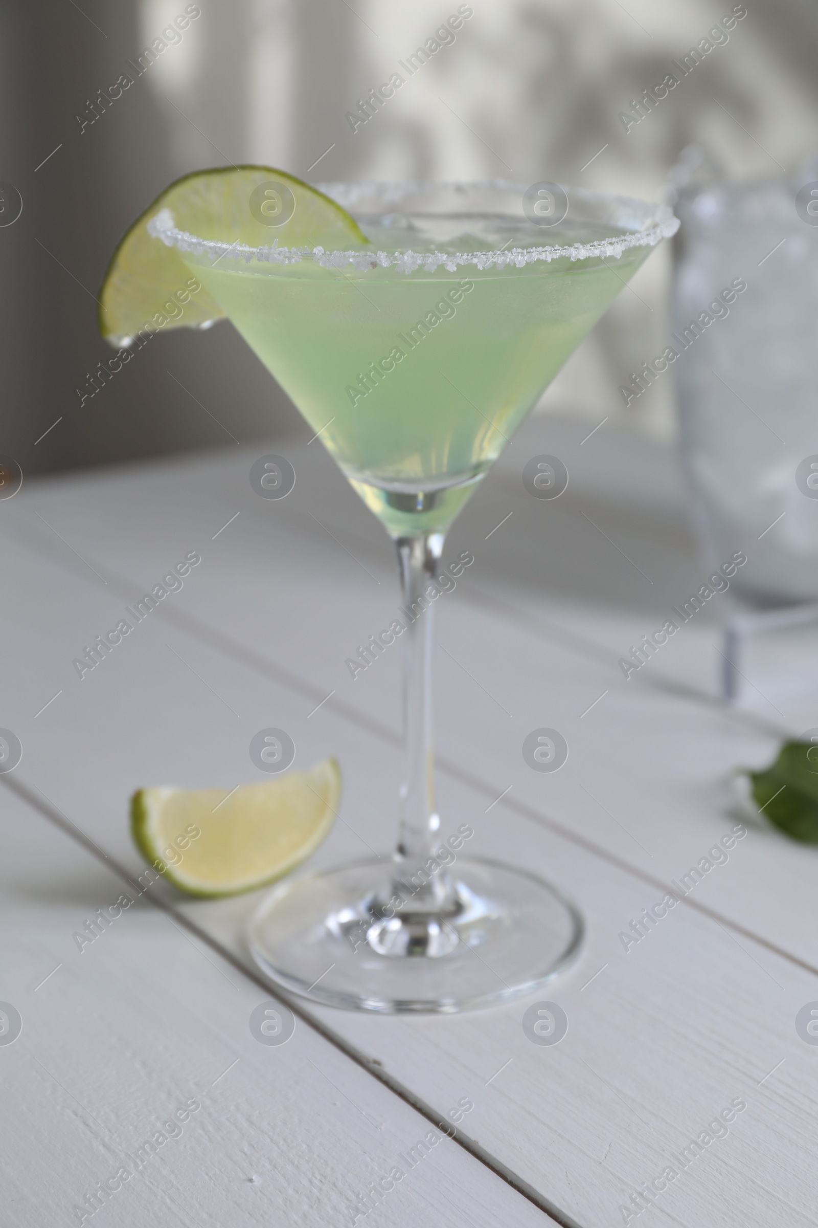 Photo of Delicious Margarita cocktail in glass and lime on white wooden table