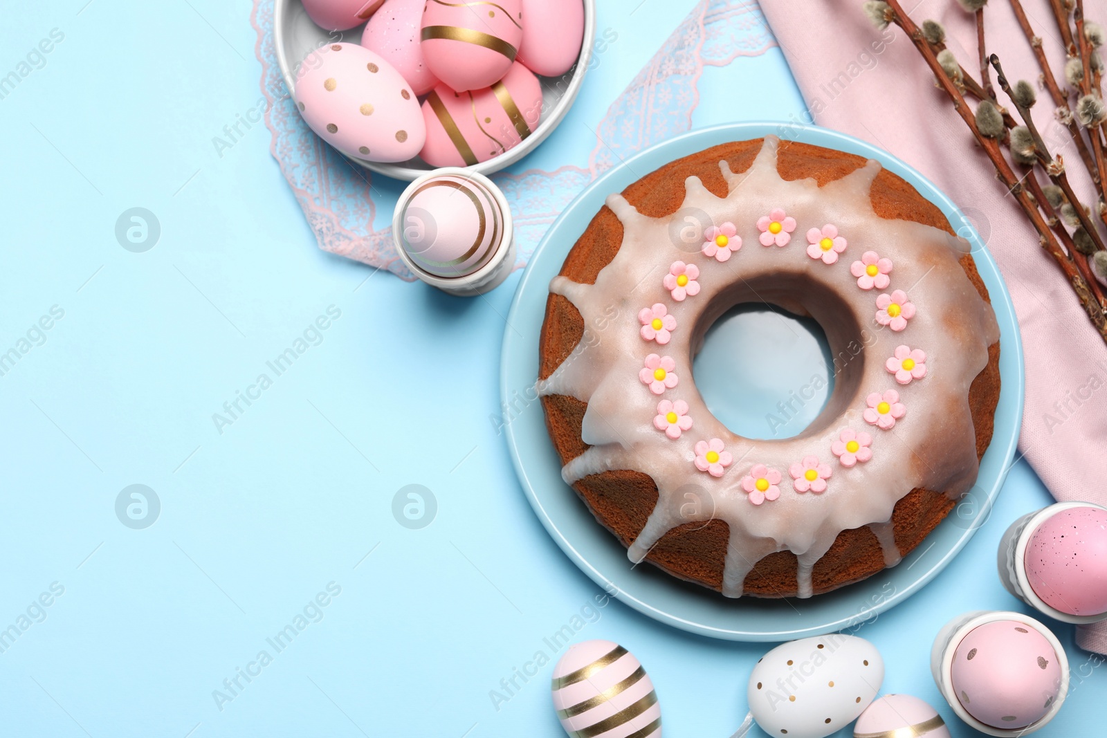 Photo of Delicious Easter cake decorated with sprinkles near painted eggs and willow branches on light blue background, flat lay. Space for text