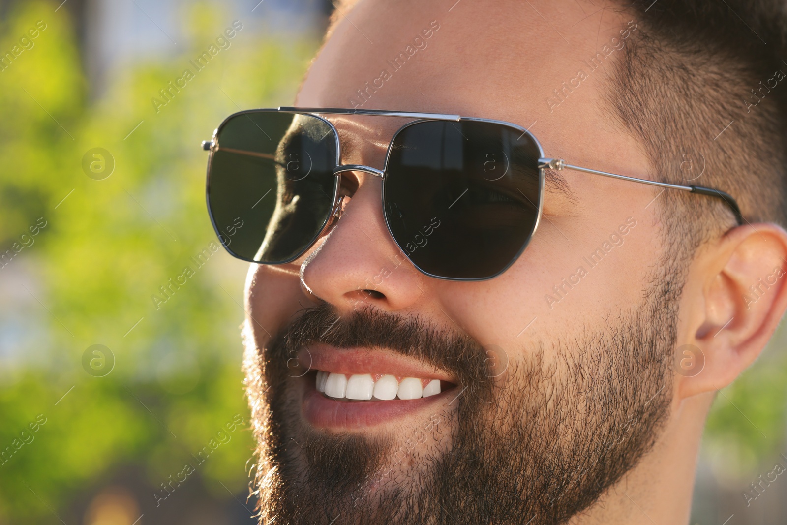 Photo of Handsome smiling man in sunglasses outdoors, closeup. Space for text