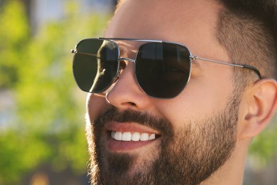 Photo of Handsome smiling man in sunglasses outdoors, closeup. Space for text