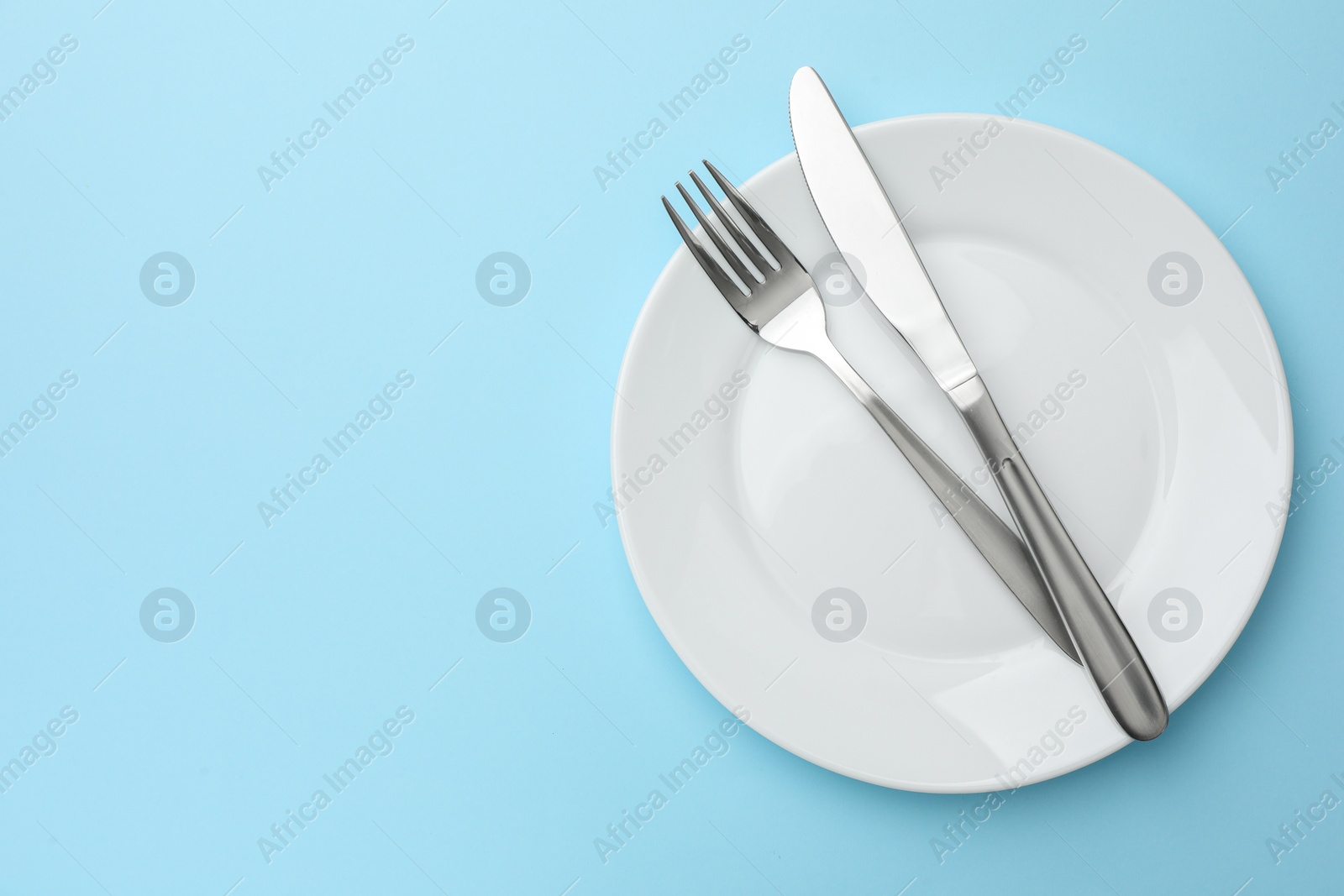 Photo of Clean plate, fork and knife on light blue background, top view. Space for text