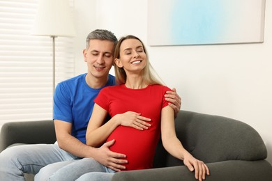 Photo of Young family housing concept. Pregnant woman with her husband on sofa at home