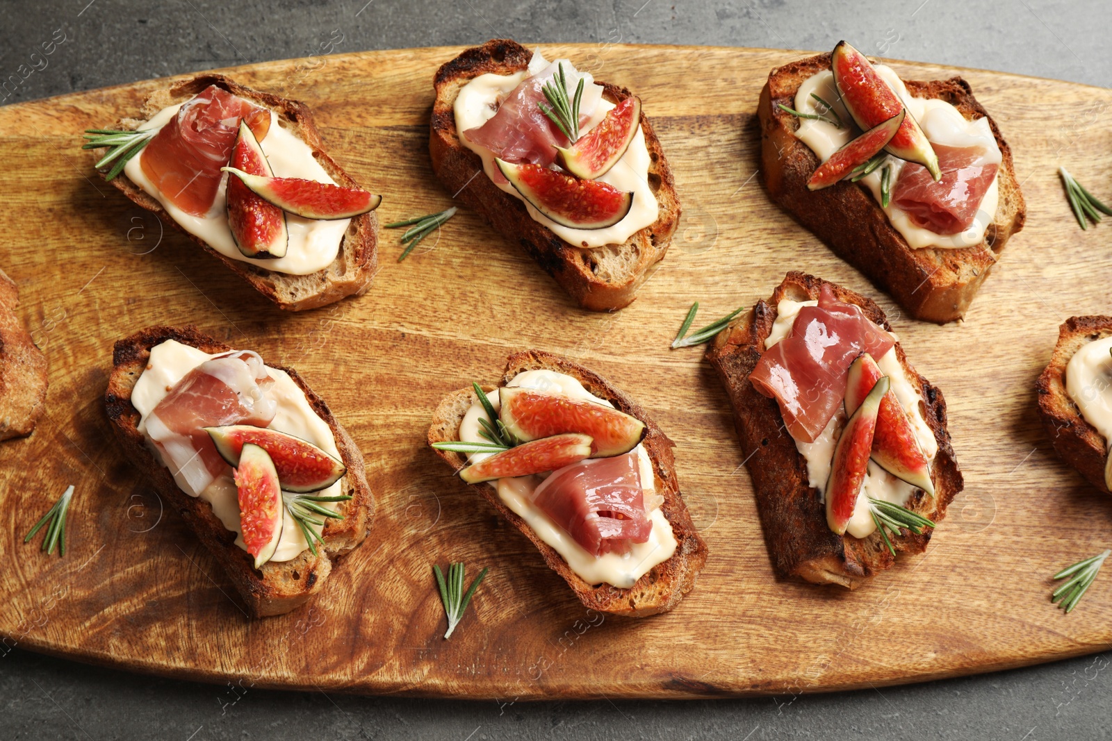 Photo of Bruschettas with cream cheese, prosciutto and figs served on wooden board, top view