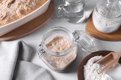 Sourdough starter in glass jar, flour and water on light table