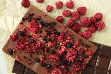 Different chocolate bars with freeze dried fruits on parchment, flat lay