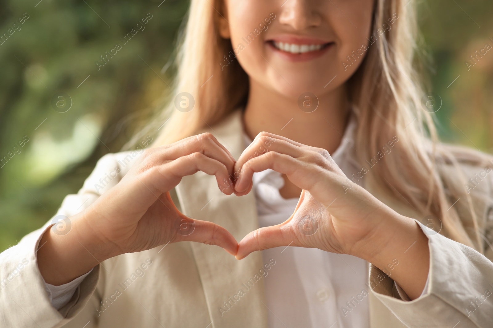 Photo of Woman showing heart gesture with hands against blurred background, closeup. Love concept