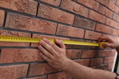 Man measuring brick wall, closeup. Construction tool