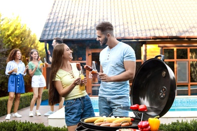 Photo of Young man and woman with grilled sausages at barbecue party outdoors