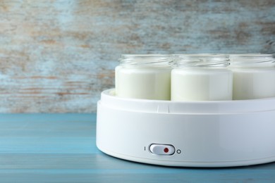 Photo of Modern yogurt maker with full jars on blue wooden table. Space for text