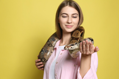 Photo of Young woman with boa constrictor on yellow background, focus on hand. Exotic pet