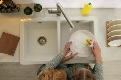 Photo of Mother and daughter washing plate above sink in kitchen, top view