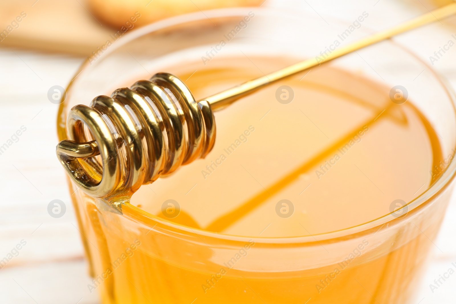 Photo of Tasty honey and metal dipper on white table, closeup