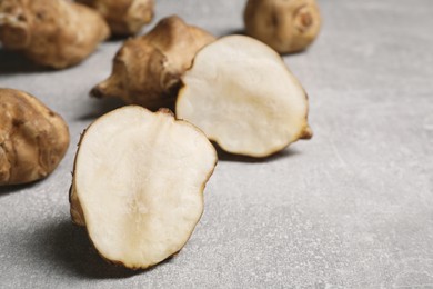 Photo of Whole and cut Jerusalem artichokes on light grey table, closeup. Space for text