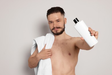 Photo of Naked man with towel and bottleshampoo on light grey background