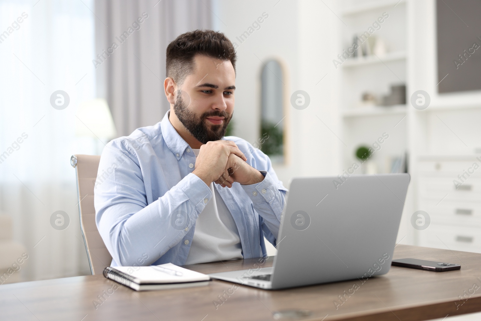 Photo of Young man watching webinar at table in room