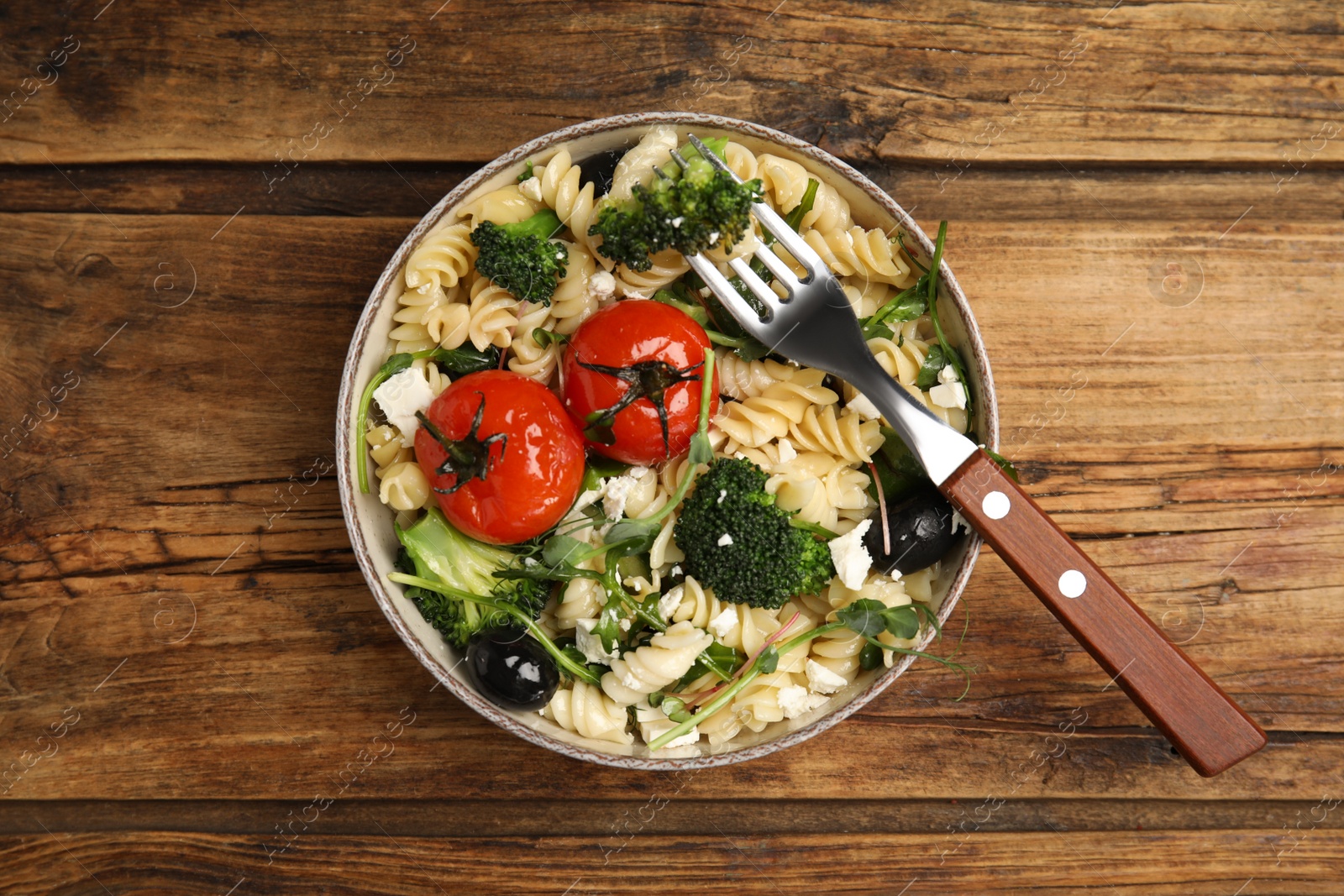 Photo of Bowl of delicious pasta with tomatoes, broccoli and cheese on wooden table, top view