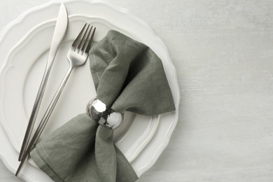 Stylish setting with cutlery, napkin and plates on light textured table, top view. Space for text