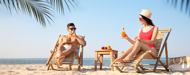 Image of Couple with drinks resting on sunny beach at resort. Banner design