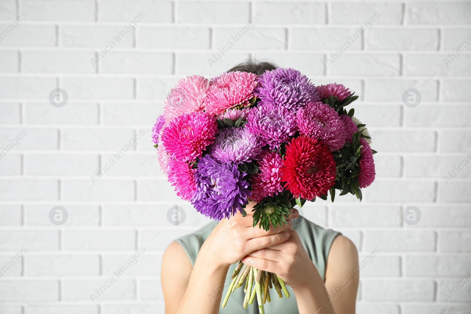 Photo of Woman holding bouquet of beautiful aster flowers against white brick wall