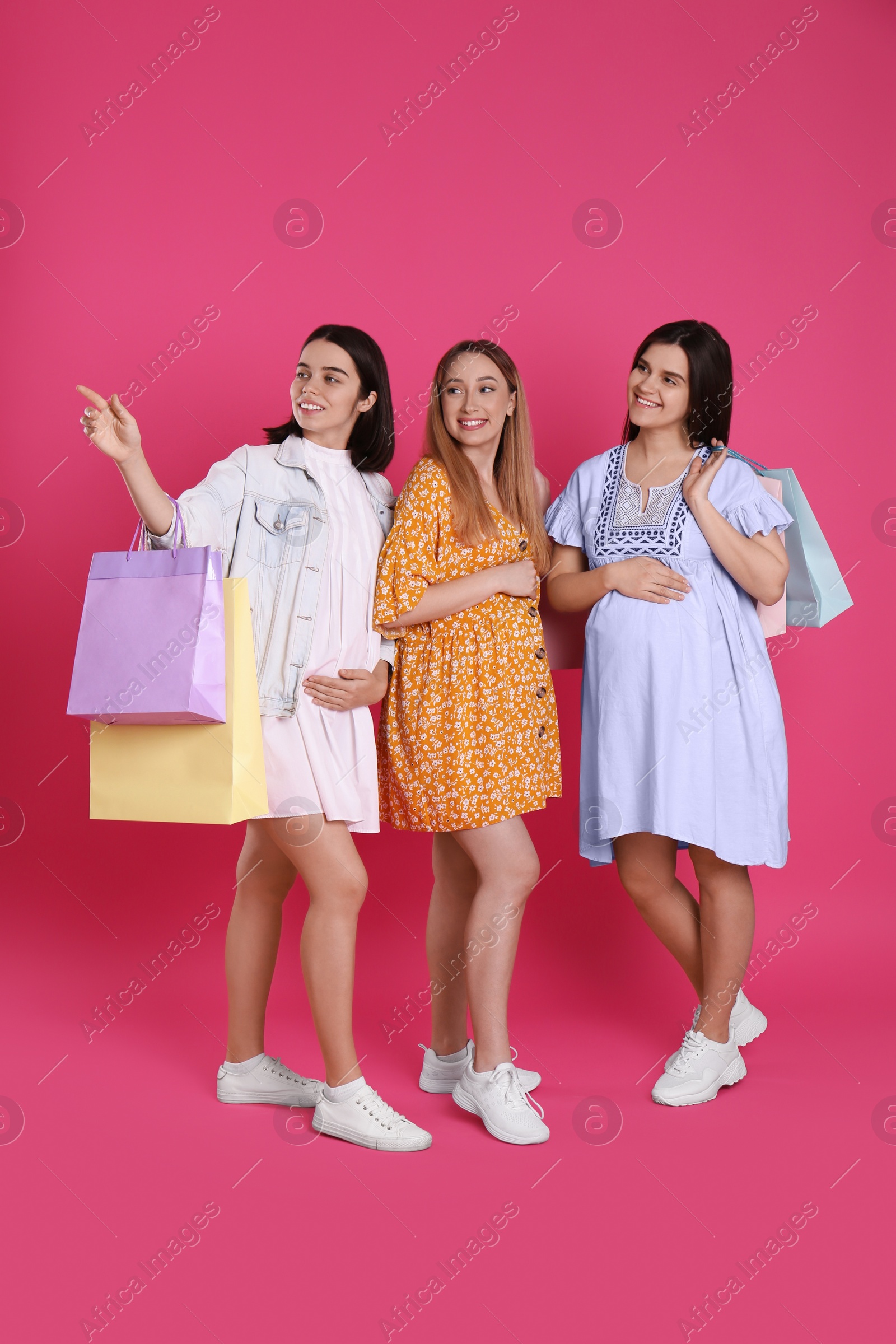 Photo of Happy pregnant women with shopping bags on pink background